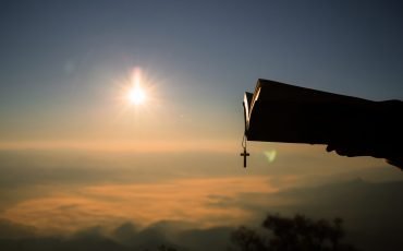 Silhouette of human hand holding bible and cross, the background Silhouette of human hand holding bible and cross, the background is the sunrise., Concept for Christian, Christianity, Catholic religion, divine, heavenly, celestial or god.